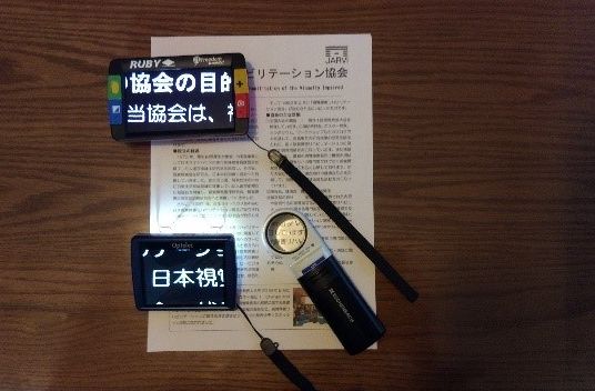 電子ルーペ(携帯型拡大読書器、左側)と光学式ルーペ(右下)